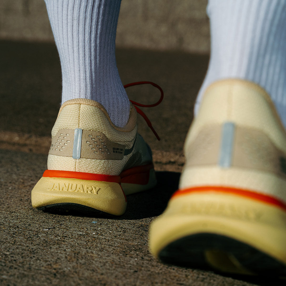 Close-up of beige running shoes with January logo showing on back on a concrete surface.